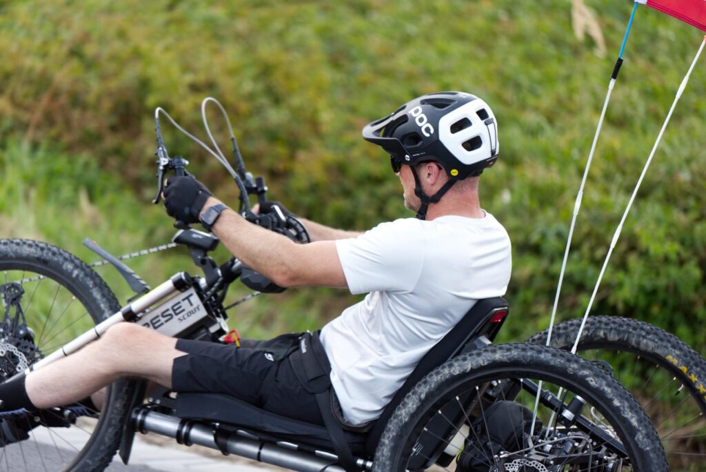 Guy biking the handbike Scout with two flags on a road