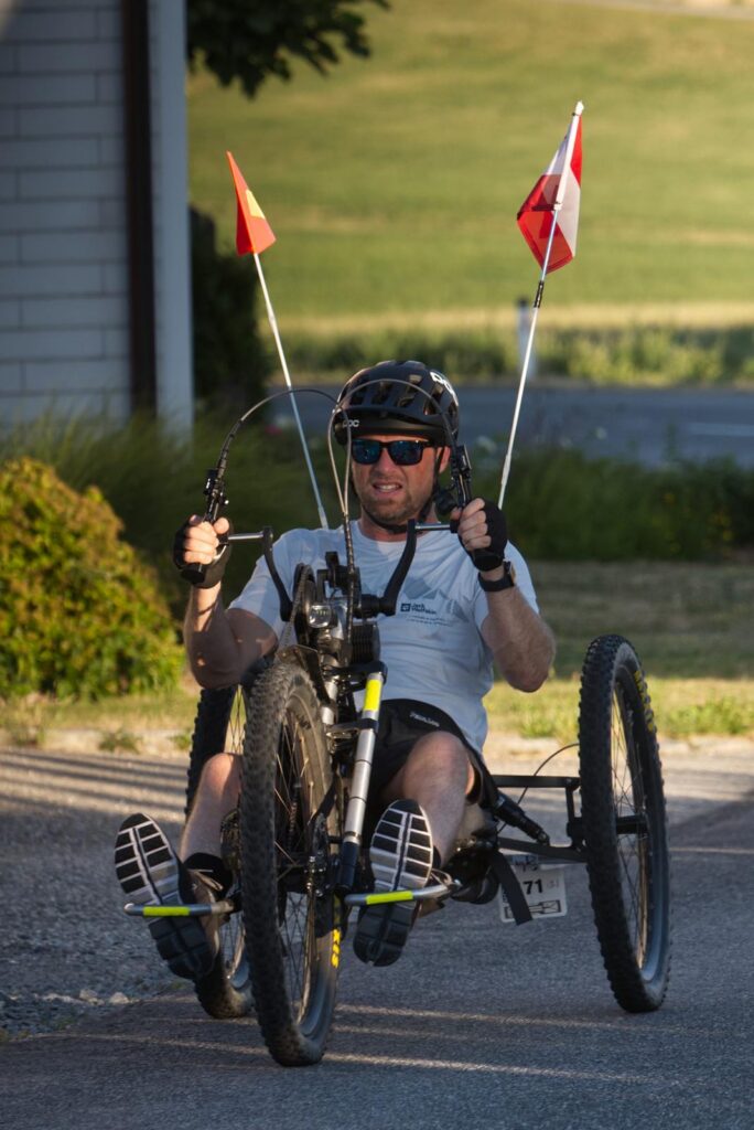 Guy biking the handbike Scout with two flags